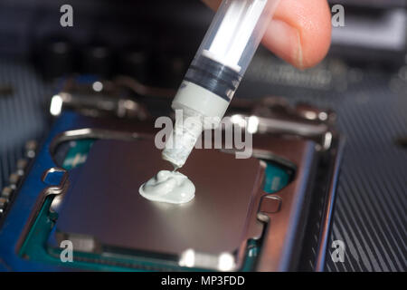 Hand mit Spritze mit Wärmeleitpaste auf der CPU Prozessor auf dem Motherboard Stockfoto