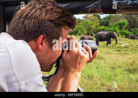 Kaukasische Mann im weißen Hemd, Fotos von Elefanten Herde während der Safari im Nationalpark von Sri Lanka Stockfoto