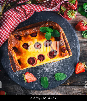 Käsekuchen mit Erdbeeren auf schwarzem Graphit Platte mit einem grünen Zweig Minze, Ansicht von oben Stockfoto