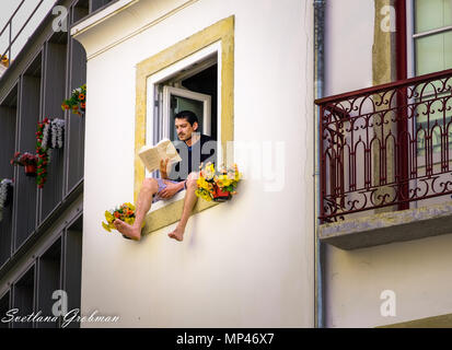 Mann sitzt auf der Abdichtung eines offenen Fensters zu lesen; die Beine des Mannes aus dem Fenster baumelt. Stockfoto