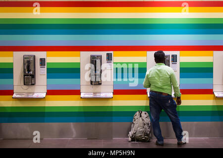 Ein indischer Mann in Jeans und Hemd, der an einer farbigen, gestreiften Telefonzelle steht, telefoniert. Singapur. Stockfoto