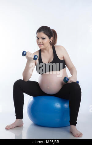 Schwangere Frau ist Übungen mit Gymnastikball auf weißem Hintergrund Stockfoto