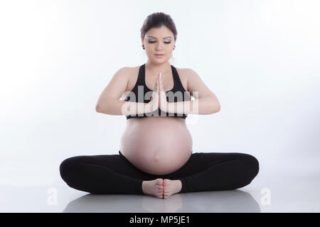 Schwangere Frau entspannen Yoga machen, sitzen im Lotussitz auf weißem Hintergrund Stockfoto