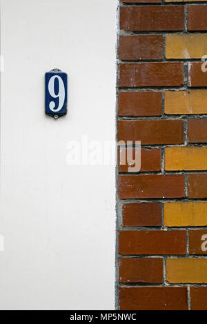 Nummer 9 auf einem blauen Fliesen gegen eine weiße Wand mit braunen Fliesen entlang der rechten Seite des Schusses. Stockfoto