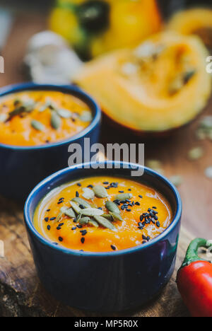 Hausgemachte Gemüsesuppe mit Kürbis, mit cremefarbenen und schwarzen Sesam, Kürbiskerne auf hölzernen Hintergrund Stockfoto