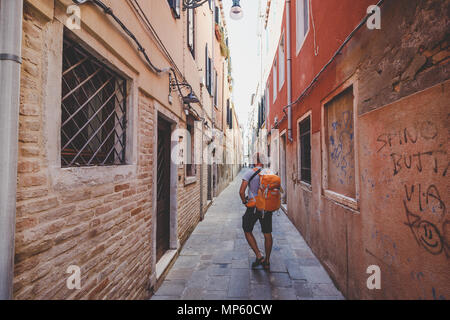 Touristen mit einem orange Rucksack und bandana Wanderungen entlang der schmalen Straße in Europa. Italien Venedig im Sommer. Die Fassade der alten Häuser ohne Menschen und c Stockfoto