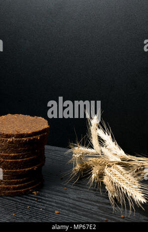 Roggenbrot, dunkle, duftende, in dünne Scheiben geschnitten auf einer hölzernen Hintergrund. Laib Brot und Roggen Ohren noch Leben auf der rustikalen Hintergrund Stockfoto