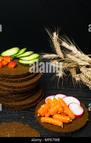 Scheibe Schwarzbrot mit einem Schnitt in der Form eines Herzens mit Gemüse - Gurken, Radieschen, rote Paprika, Karotte auf dunklem Hintergrund. Gesundheit Stockfoto