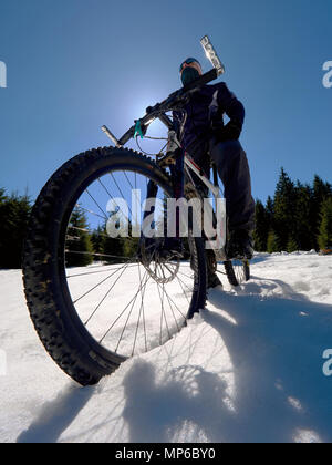 Mountainbike im gefrorenen Schnee gegen den blauen Himmel. Versteckte Asphalt unter Abdeckung säen. Extreme adrenalin Sport Stockfoto