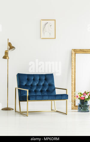 Ein luxuriöses, navy blue Sessel, goldenen Elemente, gerahmte Kunst und eine bunte Blumen Blumenstrauß in einem weißen Wohnzimmer Innenraum Stockfoto