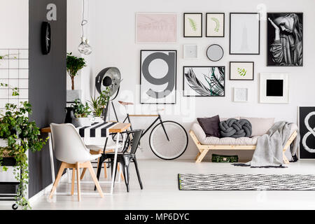 Schwarze und weiße Stuhl am Tisch im offenen Raum Interieur mit Fahrrad und Poster über beige Sofa Stockfoto