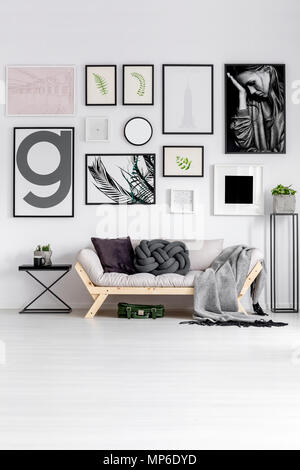 Gemusterte Decke auf Sofa gegen die Wand mit Galerie von Plakaten im hellen Wohnzimmer Innenraum Stockfoto