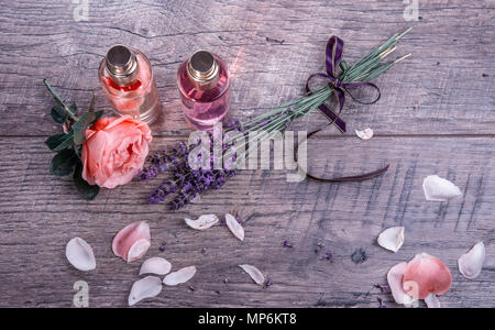 Spa mit Rosenblättern Öl, duftende Rose Wasser in Glasflaschen und Lavendel mit lila Schleife auf Holz- Hintergrund, rustikalen Stil. Massage, Aromatherapie und Naturkosmetik Konzept. Stockfoto