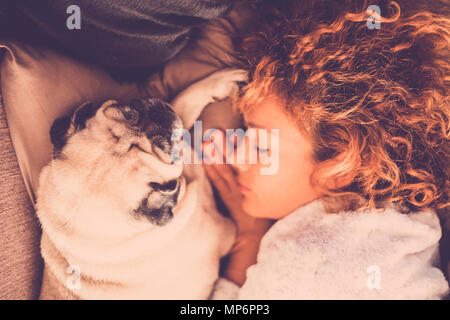 Eine Frau mit langen, lockigen Haar schlafen in eine Wolldecke mit zwei Mops Hund Stockfoto