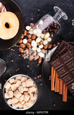 Blick von oben auf die Erdnüsse in Schokolade, auf der dunklen Kammer verschüttet, neben Schokolade Tabletten, Donuts, brauner Zucker und Kaffee Bohnen Stockfoto