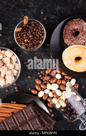 Blick von oben auf die Erdnüsse in Schokolade, auf der dunklen Kammer verschüttet, neben Schokolade Tabletten, Donuts, brauner Zucker und Kaffee Bohnen Stockfoto