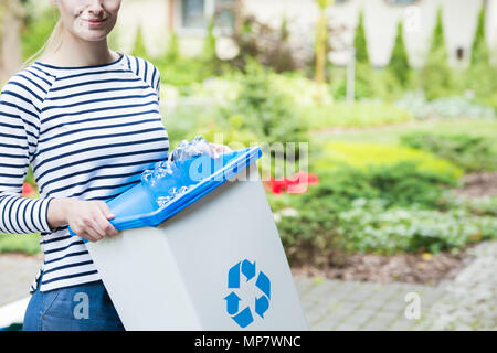 Lächelnde Frau Trennen von Kunststoff Flaschen für das Recycling bin mit blauen Symbol bestimmt Stockfoto