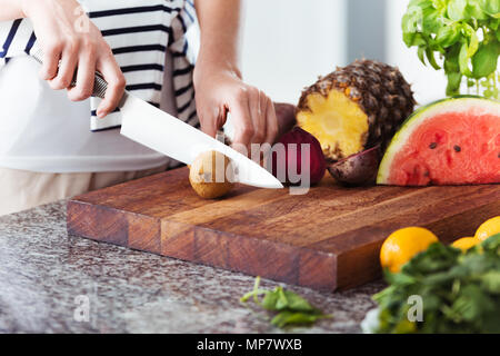 Frau auf Diät schneiden Obst auf Holzbrett in Küche mit Hochglanz Arbeitsplatte. Frugivore Diät Konzept Stockfoto