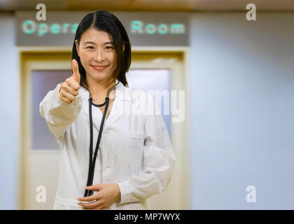 Chinesische Ärztin im Krankenhaus operation Zimmer, an der Kamera auf der Suche geben Daumen oben-Geste Stockfoto