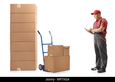 Volle Länge Profil Schuß eines Mover neben einem Hand-Lkw und ein Stapel von Kisten schreiben in Zwischenablage auf weißem Hintergrund stehend Stockfoto