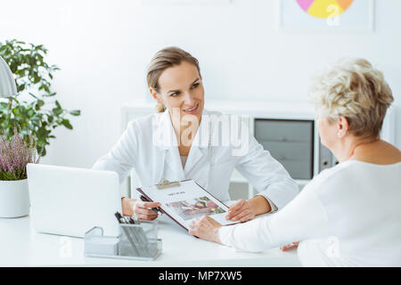 Lächelnd Ernährungsberater halten eine Diät Plan während der Konsultation mit dem Patienten im Büro mit Laptop auf dem Schreibtisch Stockfoto