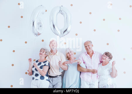 Begeisterte Senioren feiern die ältere Frau Geburtstag mit silberfarbenen Ballons Stockfoto