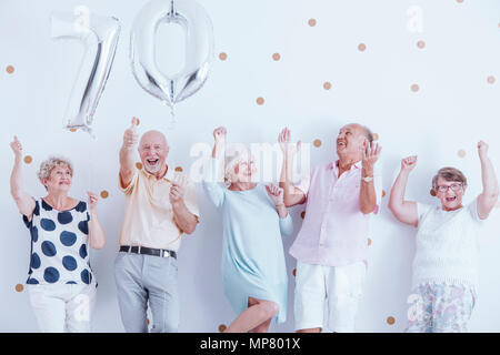 Positive Senioren Familie feiert Geburtstag des Großvaters mit silberfarbenen Ballons Stockfoto