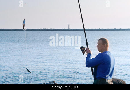 Ein Mann gefangen ein Fisch auf eine Angelrute, Angeln auf einem Salak, Angeln am Abend, Angeln im Meer im Frühling Stockfoto