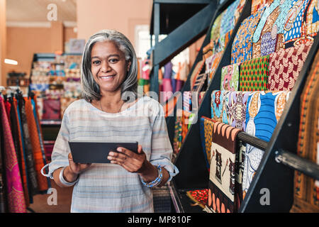 Lächelnde Frau mit einem digitalen Tablet in ihren Textilien Shop Stockfoto