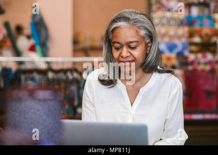Reife Frau, die an einem Notebook arbeitet in ihrem Gewebe shop Stockfoto