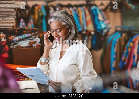 Reife Frau im Gespräch über ein Handy in Ihrem Gewebe shop Stockfoto