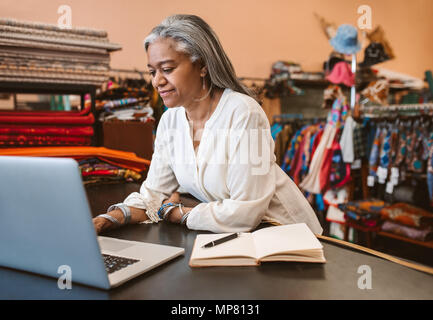 Reife Frau, die an einem Notebook arbeitet in ihren Textilien store Stockfoto