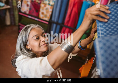 Lächelnde Frau mit Tuch Rollen in einem Stoff Shop suchen Stockfoto