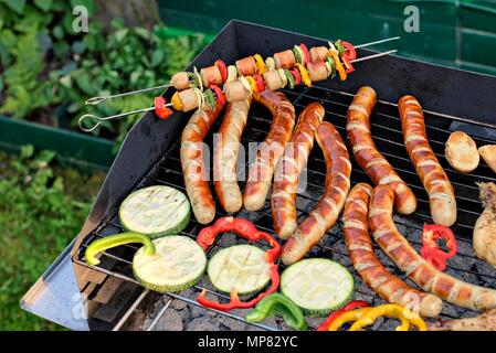Leckeres Essen, Ernährung, kulinarischen und Grill Konzept: gegrillte Würstchen, Hähnchen Schenkel und Gemüse auf einem Grill. Stockfoto