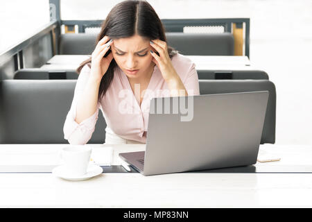 Eine müde Frau ihren Kopf vor ihrem Laptop, Kopfschmerzen und der Arbeit erschöpft. Stockfoto