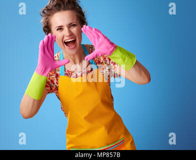 Große Reinigung Zeit. glückliche junge Frau mit gummihandschuhe Schreien über Megaphon geformten Hände isoliert auf Blau Stockfoto