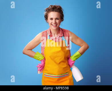 Große Reinigung Zeit. Glücklich moderne Frau in einem gelben Schürze mit Küche, Schwamm und Reinigungsmittel isoliert auf Blau Stockfoto