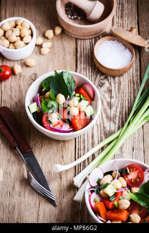 Frisches Gemüse Salat mit Kichererbsen, Rettich, Tomaten, Paprika, Gurken und Spinat in Keramik Schüssel, gesunde vegane Mahlzeit auf rustikalen Holztisch Stockfoto