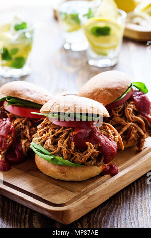 Gezogene Schweinefleischsandwiche mit Gemüse, Tomaten auf Holzbrett auf Picknick Tisch Stockfoto