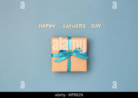 Happy Vatertag Karte mit Geschenkbox in Kraftpapier mit Blue Ribbon in Polka Dots auf blauem Hintergrund grau Band umwickelt. Grußkarte mit Holz- briefe. Stockfoto