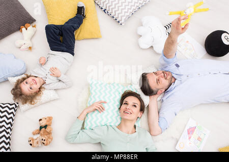 Schuss eine junge Familie mit einem Kind auf dem Boden liegend unter Kissen und Maskottchen, von oben gesehen Stockfoto