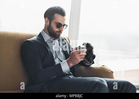 Junge stilvolle Geschäftsmann Führer drinnen im Büro tragen Sonnenbrillen Kontrolle der Fotos auf der Kamera Stockfoto