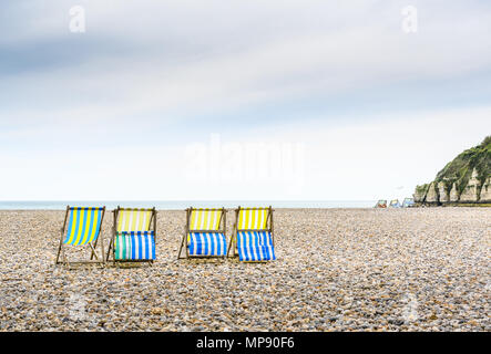 Vier Leere Liegestühle auf dem Kiesstrand vor dem kreidefelsen der Jurassic Coast im Dorf Bier, Devon, England. Stockfoto