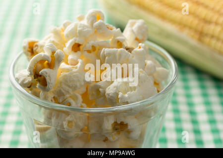 Popcorn auf Glasschale und Grüne Plaid Tabelle. Essen von Festa Junina, eine typisch brasilianische Party, Urlaub Veranstaltung im Juni. Defokussierten Maiskolben im backgro Stockfoto