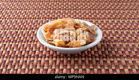 Eine kleine Schüssel mit Scheiben getrocknet Mandarinen auf einem bunten Tischset gefüllt. Stockfoto