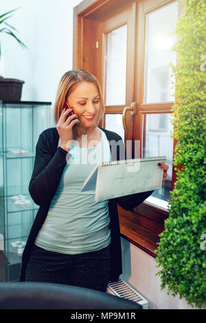 Wunderschöne reife erfolgreiche weibliche Unternehmer sprechen über ein Smartphone im Büro und dem Tag der Hauptversammlung. Stockfoto