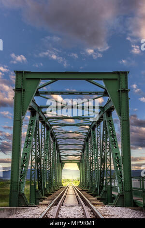 Licht am Ende des Tunnels - vertikale Ansicht durch alte, Bügeleisen, Eisenbahnbrücke bei Sonnenuntergang mit dramatischen, bunten Wolken und andere sonnenbeschienenen Seite Stockfoto