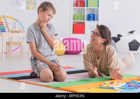 Aufnahme eines Denkens kleiner Junge sitzt auf einem Teppich neben seinem Haus Lehrer Stockfoto