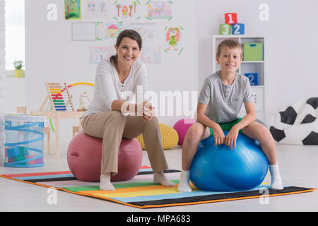 Aufnahme einer jungen Frau und einen kleinen Jungen sitzen auf Übungskugeln in einem Zimmer Stockfoto
