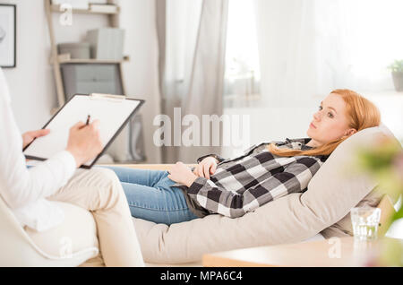 Deprimiert liegende Frau auf Sofa während der Psychotherapie, Psychologe Notizen in Ihren medizinischen Chart Stockfoto